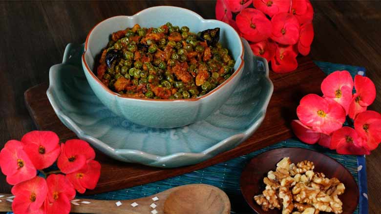 Malvani green peas and walnut curry is served in a blue celadon bowl lying on a blue celadon scalloped lotus platter with california walnuts and red flowers in the background - Malvani Green Peas and Walnut Curry Recipe